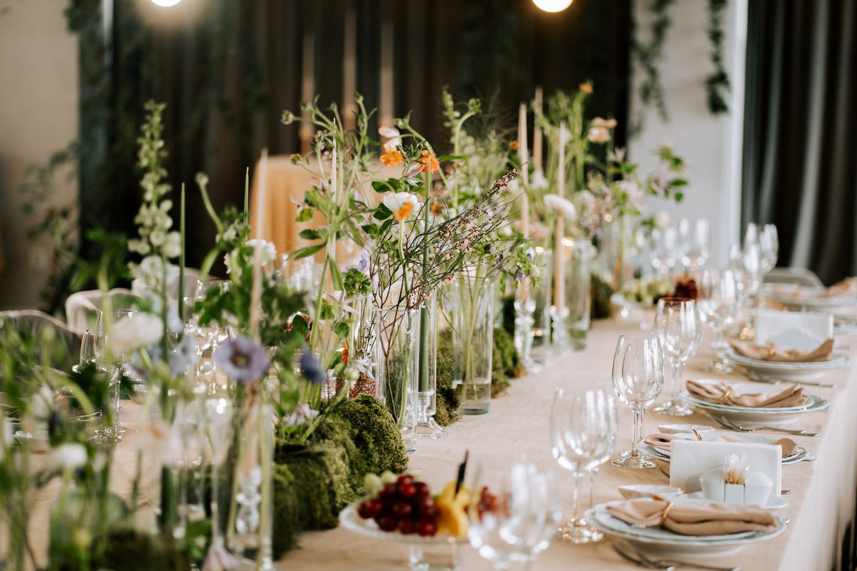Long wedding reception table set with glass bud vases, taper candles and greenery